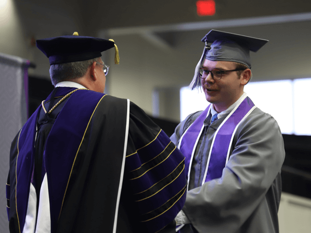 身穿灰色毕业服的男生在毕业舞台上与校长握手并领取毕业证书